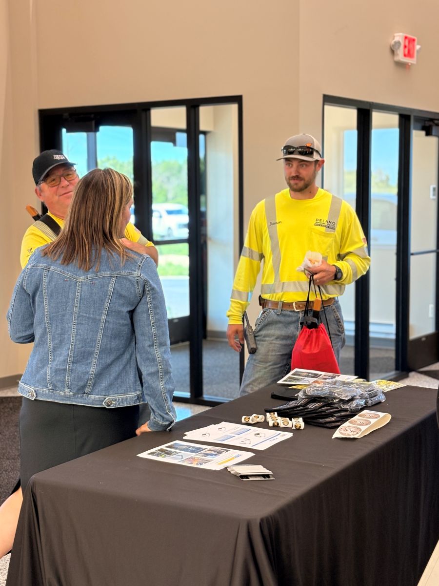 2 attendees stand at the welcome table with an Olsen employee